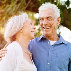 Total Well-being – Middle-aged couple laughing together under a tree