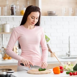 Elevates Nutrient Absorption – Woman cutting a cucumber and other vegetables in a white kitchen