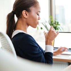 Enables Energy Levels – Woman drinking a glass of water at her desk