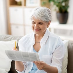 Support Your Brain – Middle-aged woman sitting on couch solving newspaper puzzles