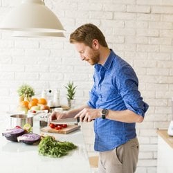 Stomach Issues – Man chopping vegetables on a cutting board in a white kitchen