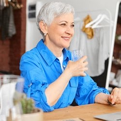 It’s Easy – Older woman drinking a glass of water in front of her laptop in a hotel room