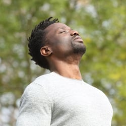 A man with eyes closed and head slightly tilted back taking a deep breath with the sun shining on his face.